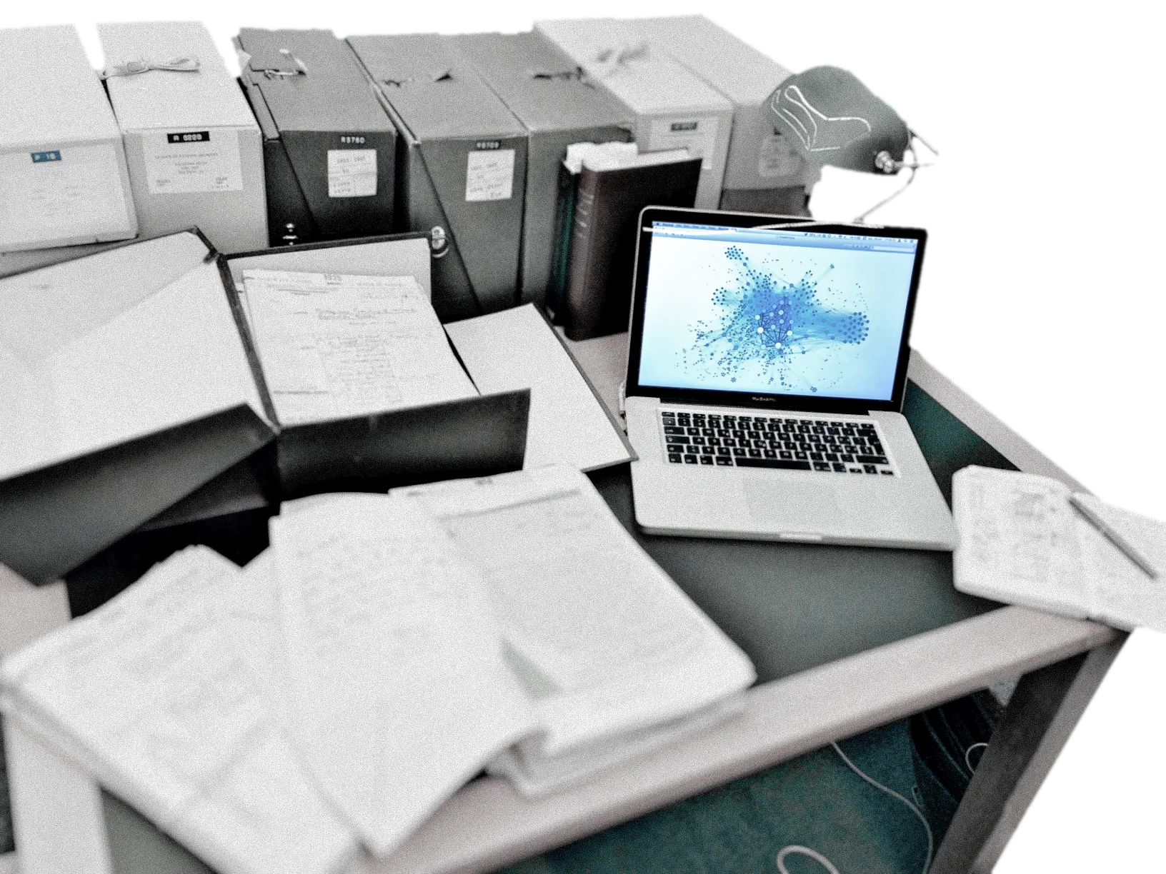 One computer, on an academic desk with archive box and notebook, shows the Gephi desktop software on its screen